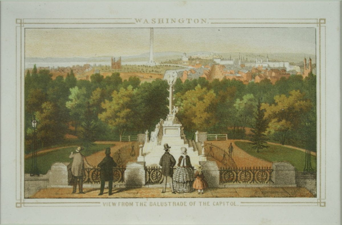 The Tripoli Monument sits on Capitol Hill with a view of DC in the background. Finely dressed visitors stand in the foreground.