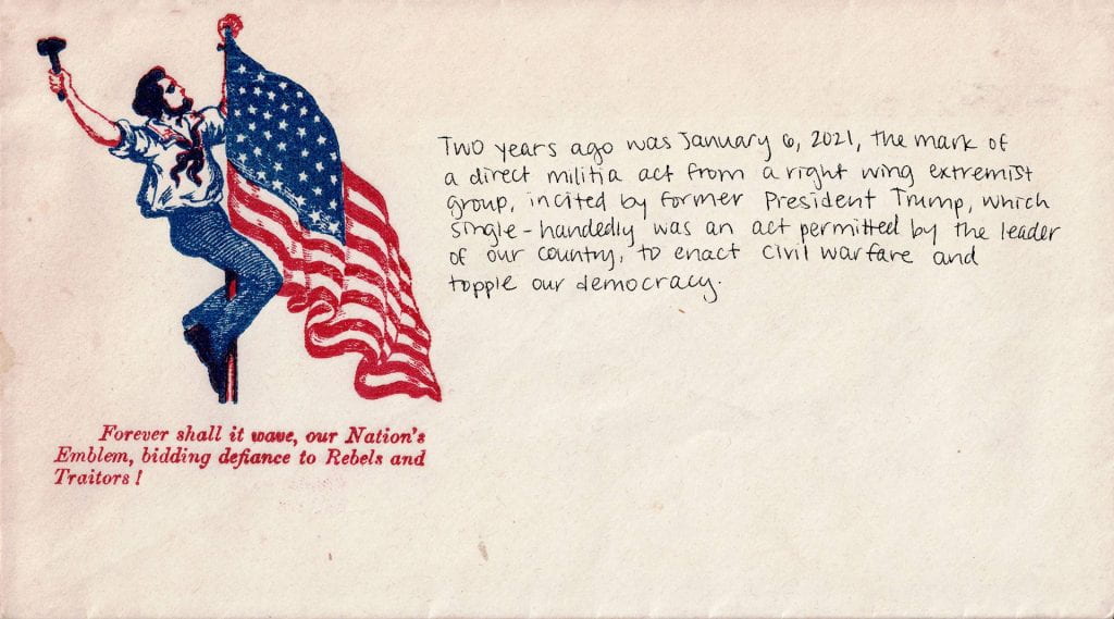 Historical envelope shows an image of a man climbing an American flag and waving a hammer or mallet in his right hand. There is red text beneath the image: "Forever shall it wave, our Nation's Emblem, bidding defiance to Rebels and Traitors!" Handwritten, contemporary text reads: "Two years ago was January 6, 2021, the mark of a direct militia act from a right wing extremist group, incited by former President Trump, which single-handedly was an act permitted by the leader of our county, to enact civil warfare and topple our democracy.