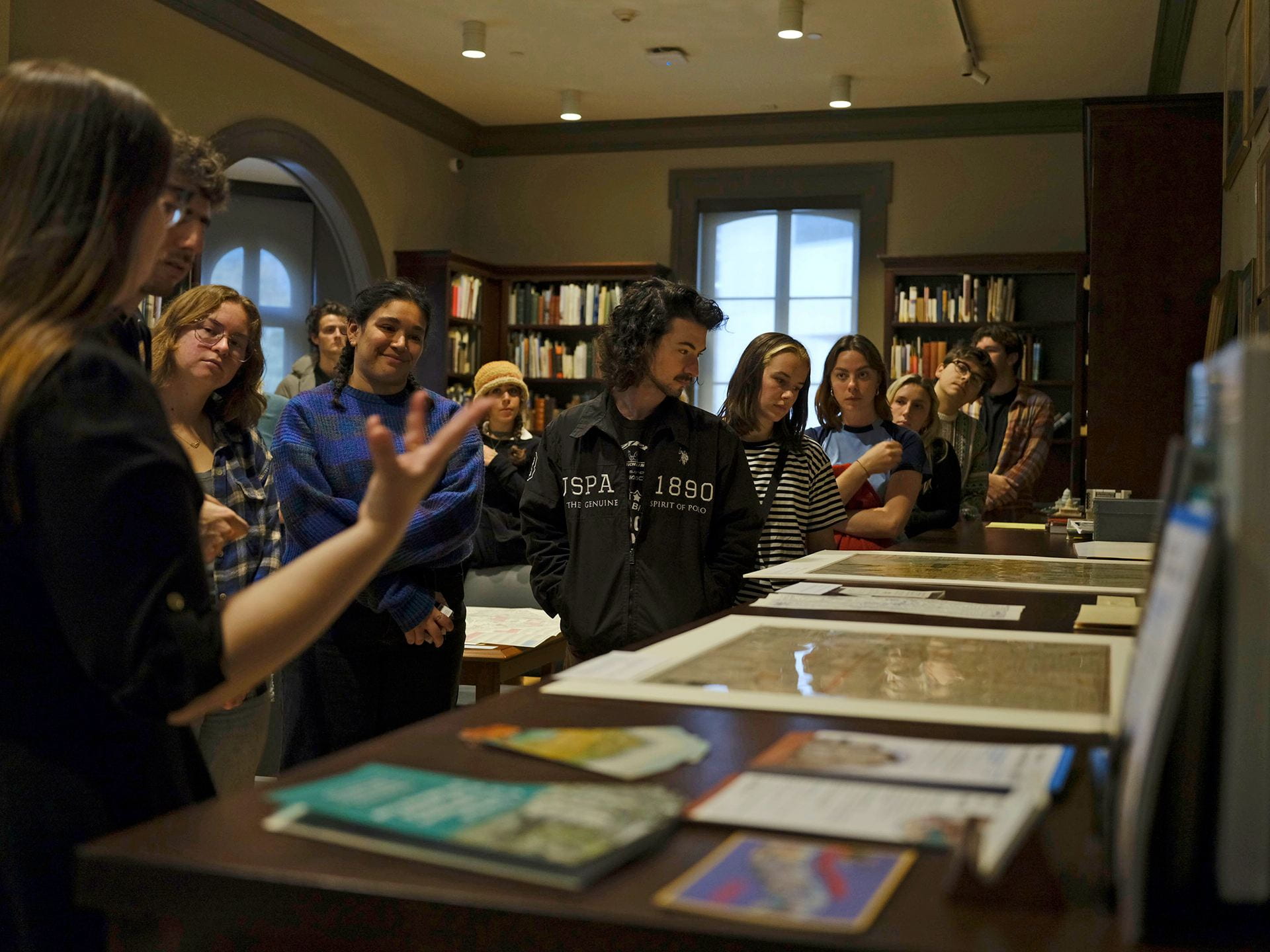 A group of college students gather around a display of historical prints