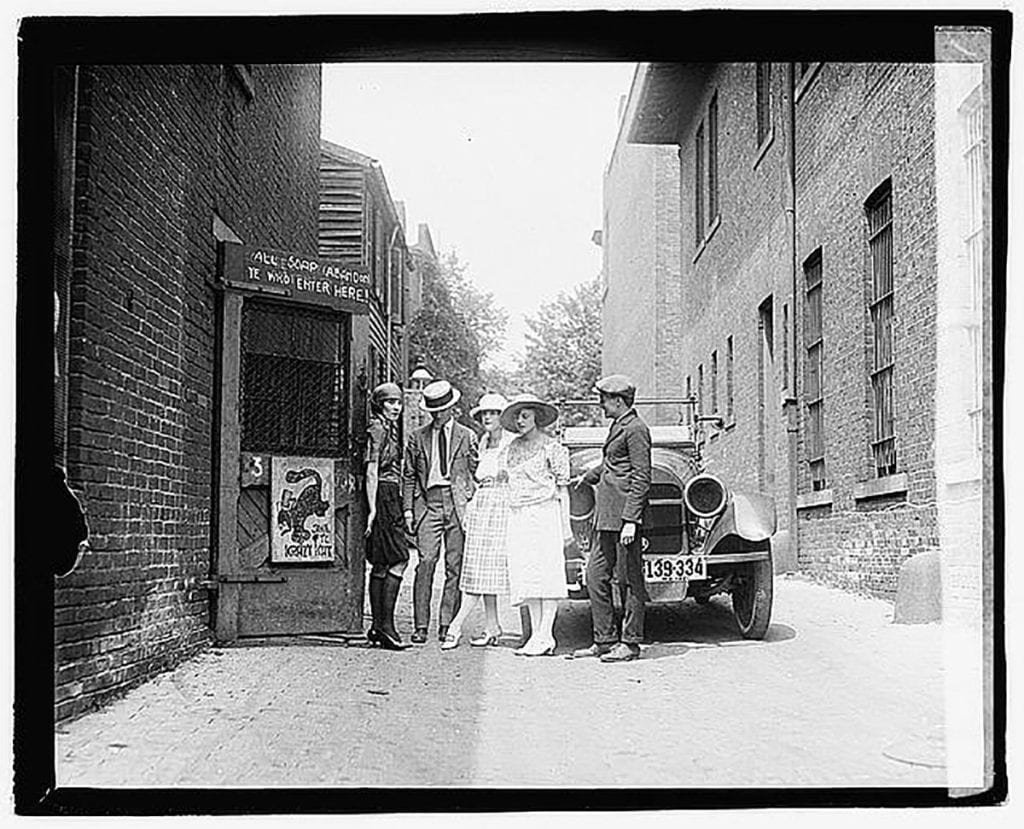 Group of people standing in front of car parked in an alleyway